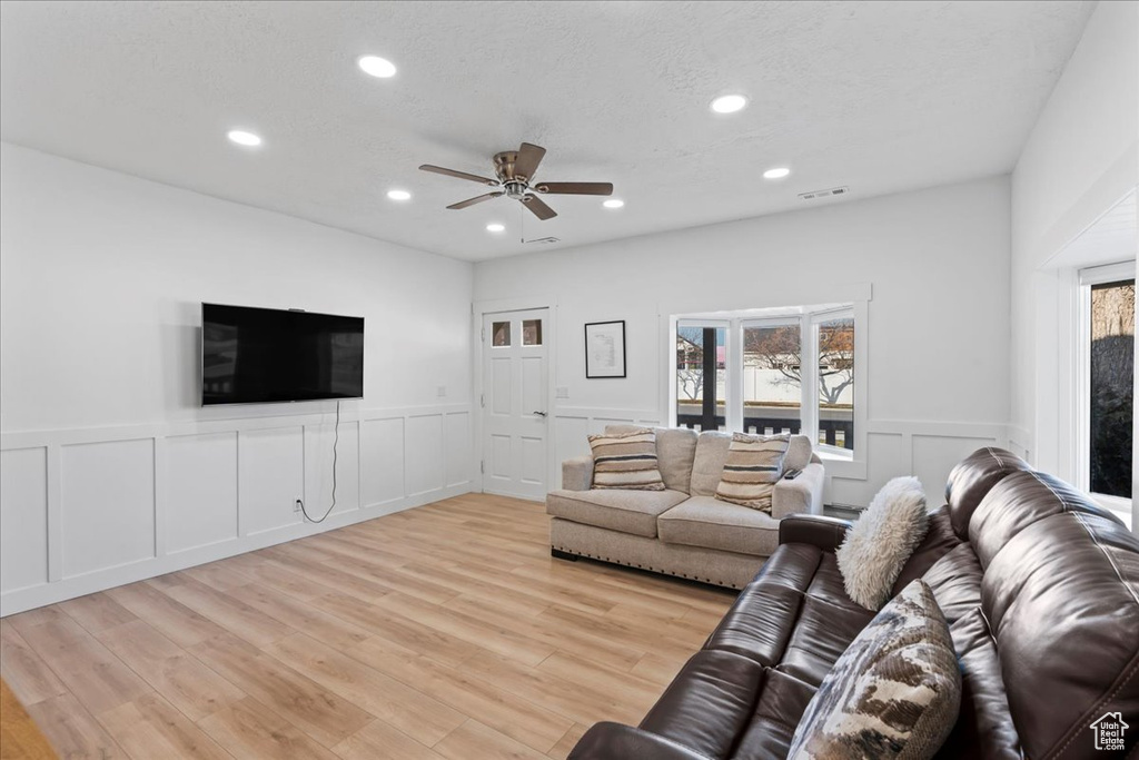 Living room with ceiling fan, light wood-type flooring, and a textured ceiling