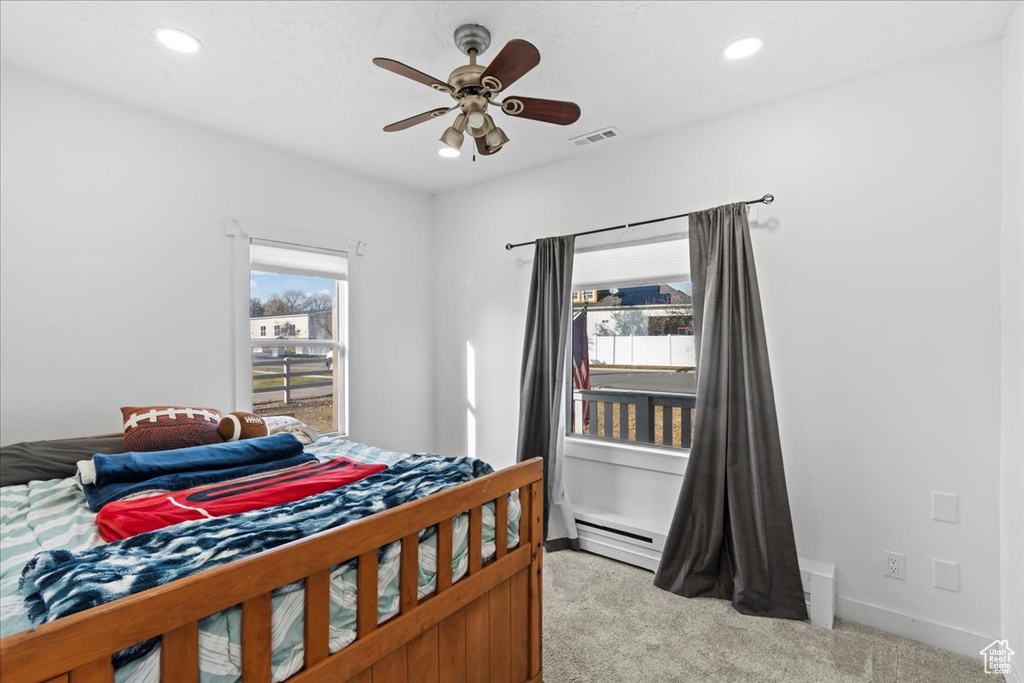 Carpeted bedroom featuring multiple windows, ceiling fan, and a baseboard radiator