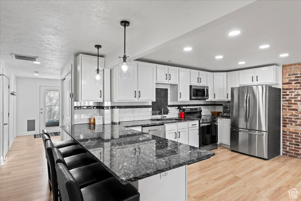 Kitchen with pendant lighting, kitchen peninsula, light wood-type flooring, and stainless steel appliances