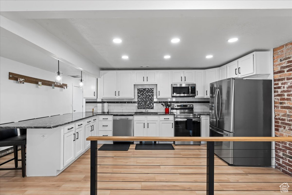 Kitchen with a kitchen bar, white cabinets, stainless steel appliances, and light hardwood / wood-style floors