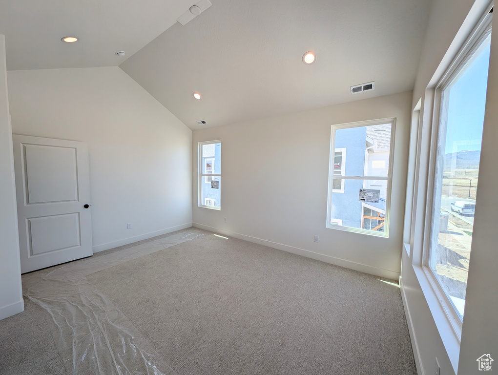 Unfurnished room featuring carpet floors, baseboards, visible vents, and lofted ceiling