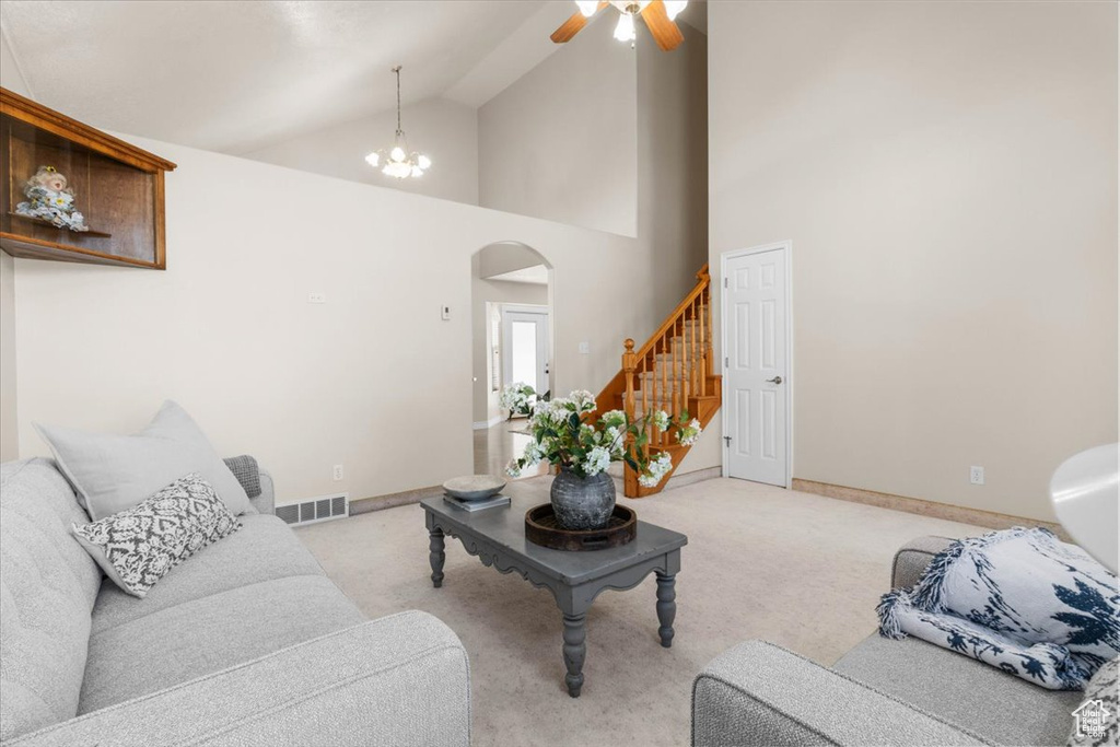 Living area featuring arched walkways, light carpet, ceiling fan, baseboards, and high vaulted ceiling