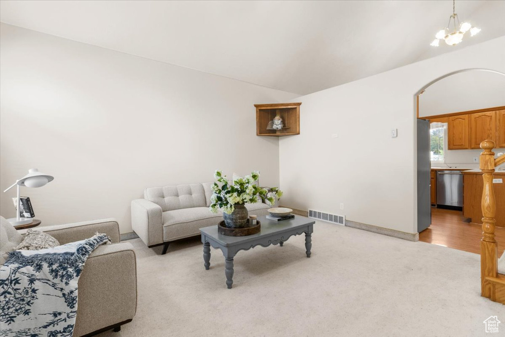 Living area with a chandelier, light colored carpet, lofted ceiling, and baseboards