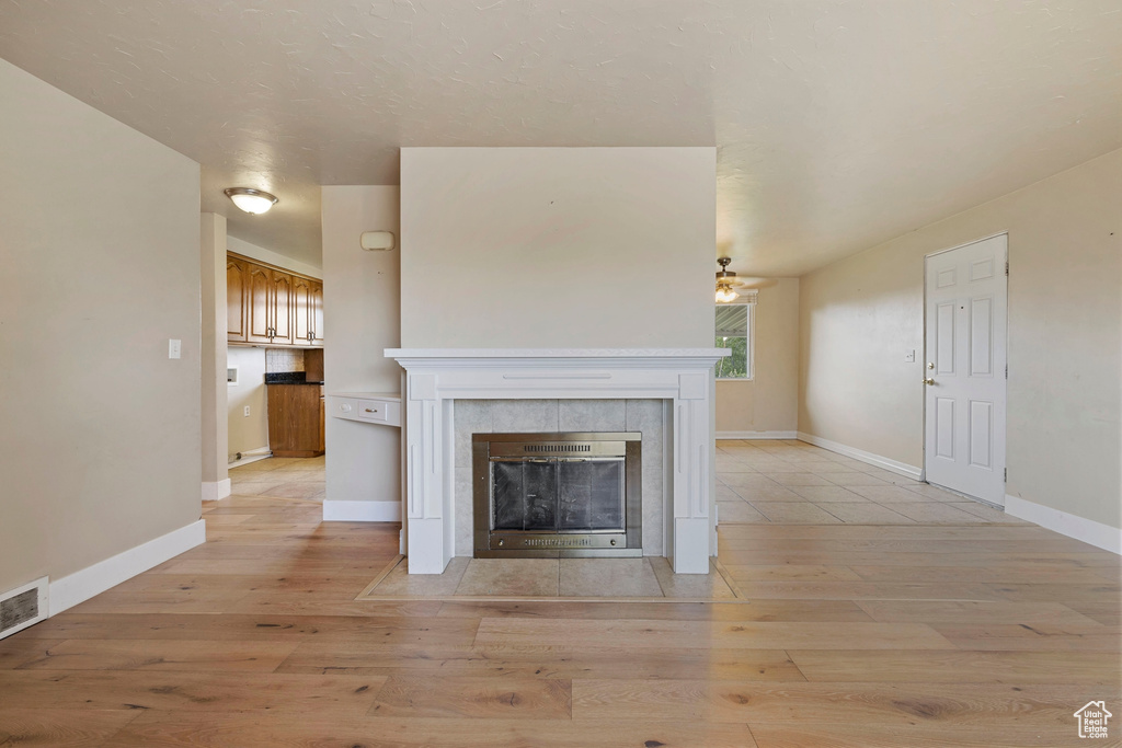Unfurnished living room featuring a tile fireplace, light hardwood / wood-style floors, and ceiling fan