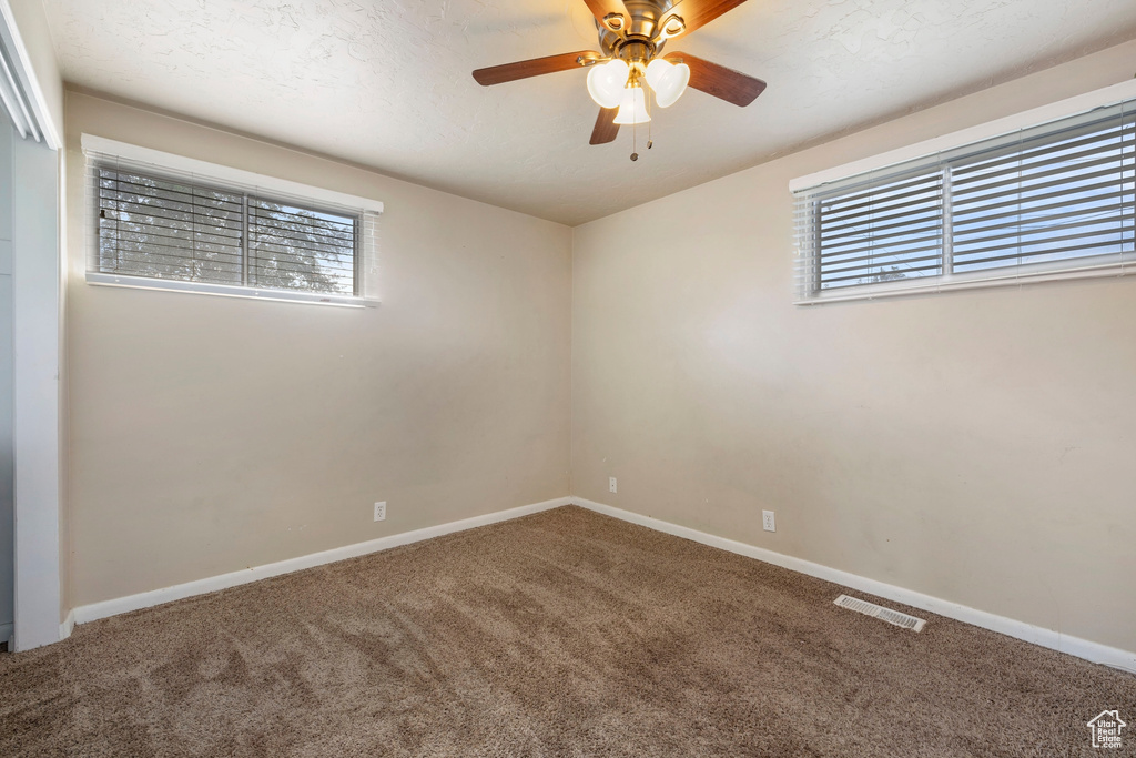 Empty room with ceiling fan, carpet floors, and a textured ceiling