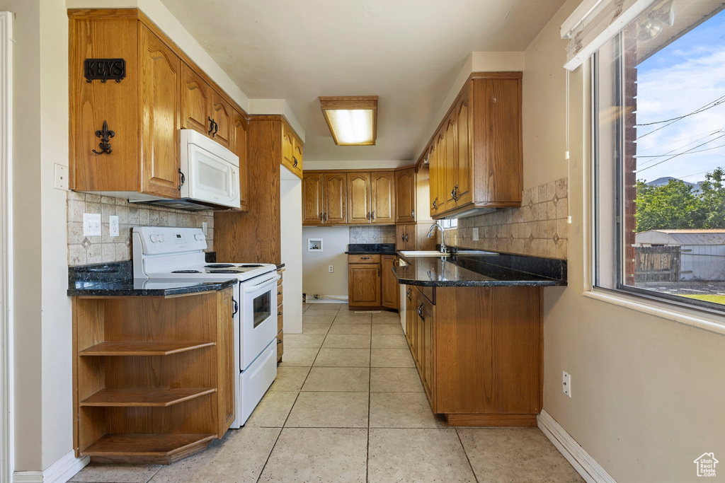 Kitchen with dark stone countertops, decorative backsplash, light tile patterned flooring, and white appliances