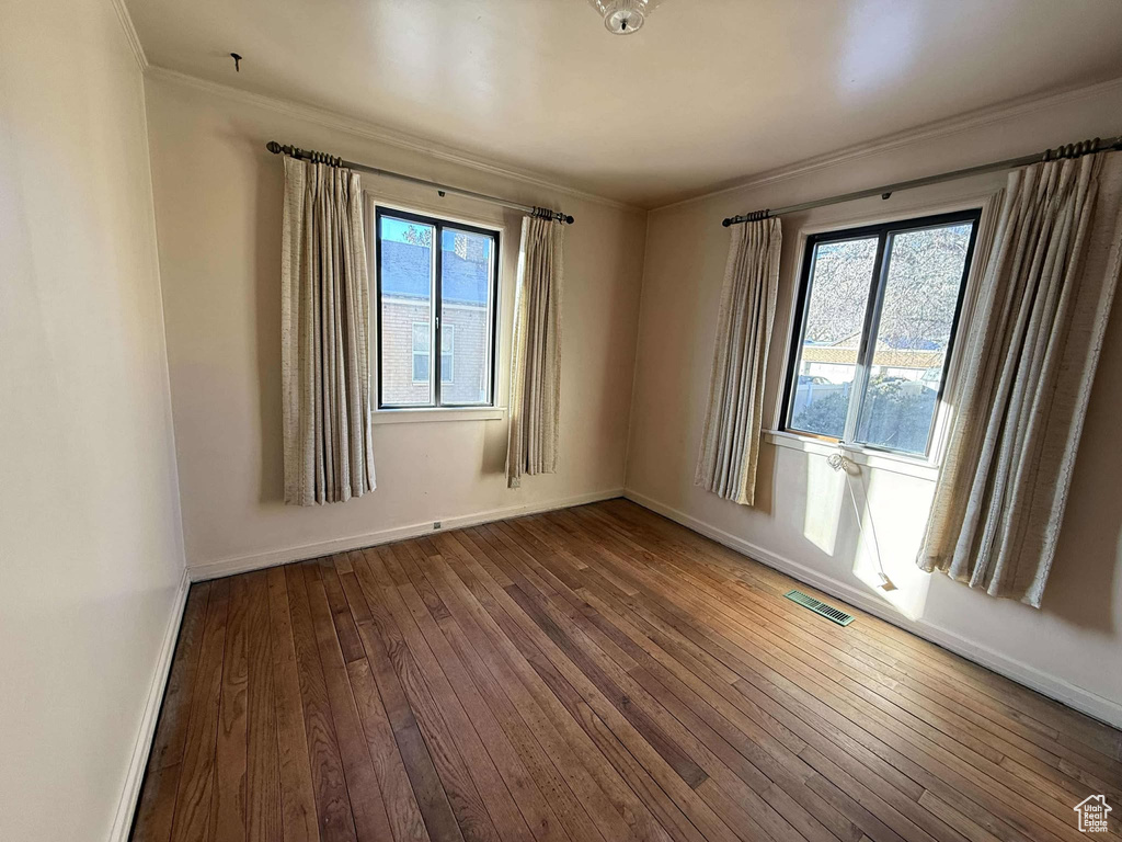 Unfurnished room with hardwood / wood-style floors, a healthy amount of sunlight, and ornamental molding