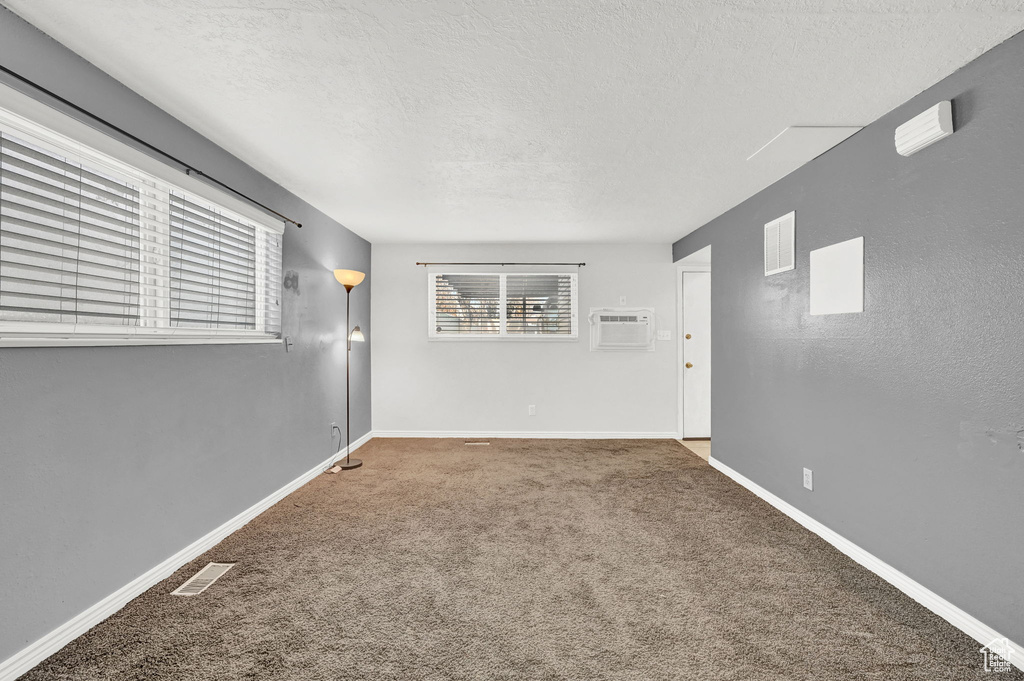 Carpeted spare room with a wall unit AC and a textured ceiling