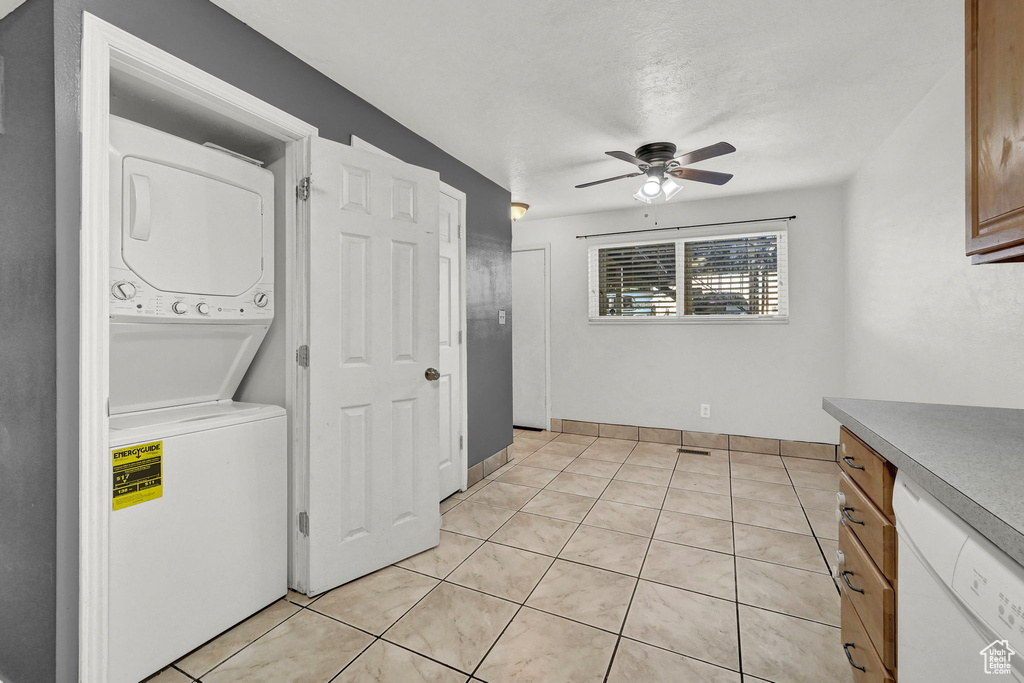 Laundry area featuring ceiling fan, stacked washer and clothes dryer, and light tile patterned flooring