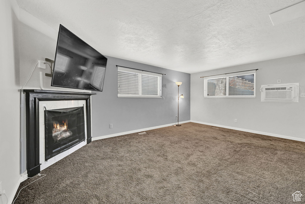 Unfurnished living room featuring a wall unit AC, a tiled fireplace, carpet flooring, and a textured ceiling