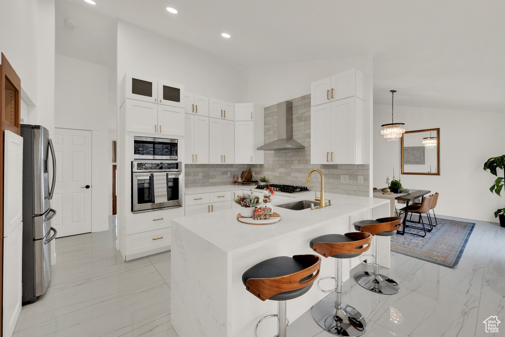 Kitchen with wall chimney exhaust hood, a breakfast bar, stainless steel appliances, sink, and hanging light fixtures