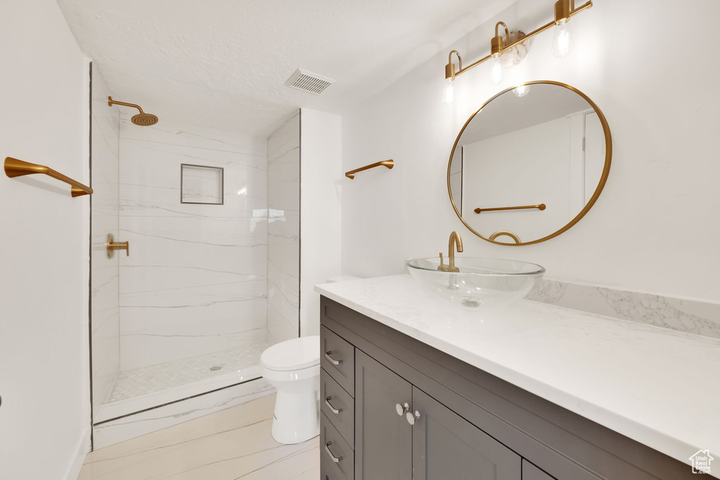 Bathroom with tiled shower, vanity, and toilet