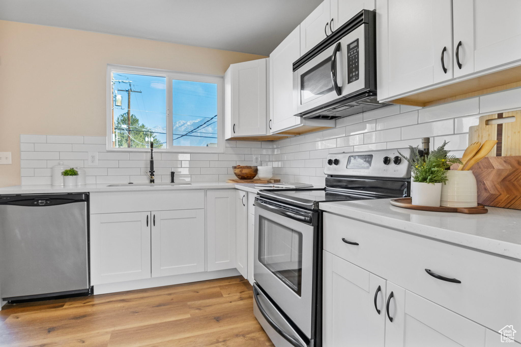 Kitchen with sink, stainless steel appliances, light hardwood / wood-style floors, decorative backsplash, and white cabinets