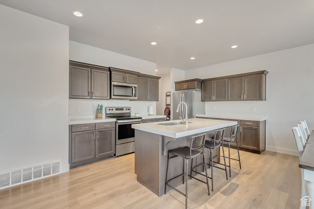 Kitchen featuring appliances with stainless steel finishes, light wood-type flooring, a breakfast bar, a kitchen island with sink, and sink