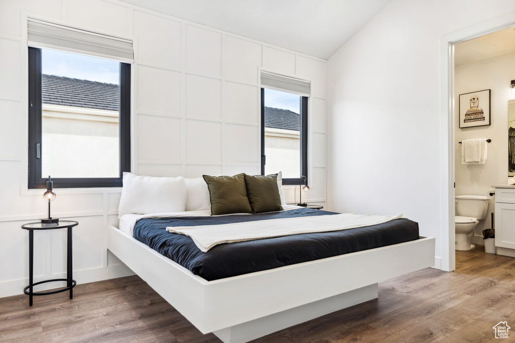 Bedroom featuring hardwood / wood-style floors, vaulted ceiling, connected bathroom, and multiple windows