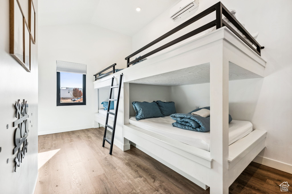 Bedroom with vaulted ceiling, wood-type flooring, and a wall mounted AC