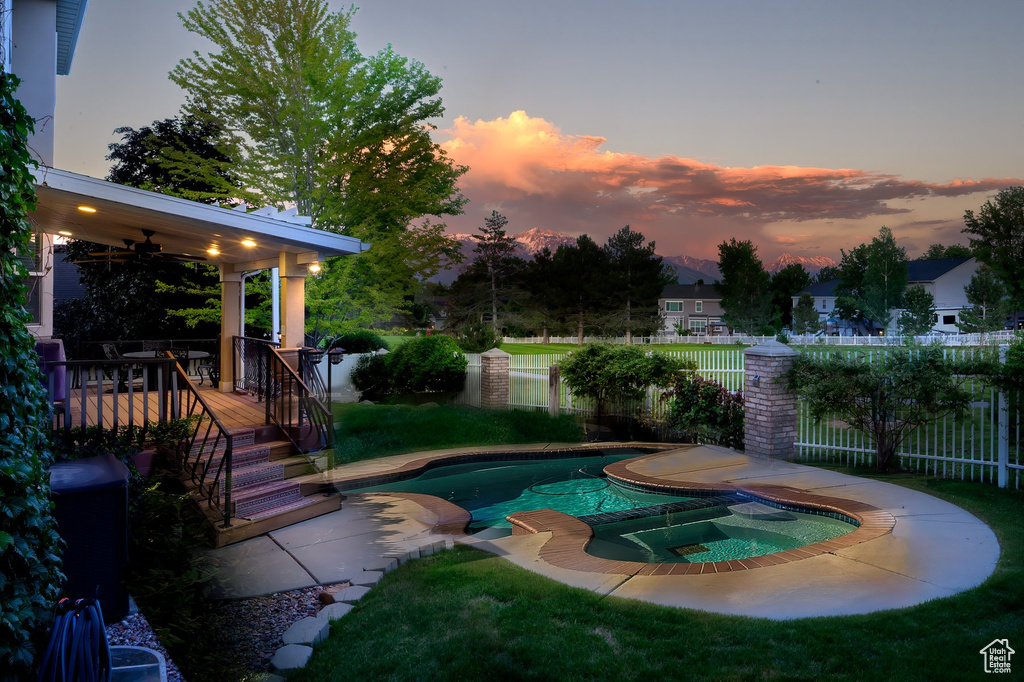 Pool at dusk featuring a ceiling fan and a pool with connected hot tub