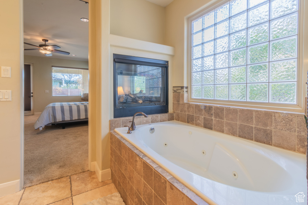Bathroom with tiled bath, ceiling fan, and a healthy amount of sunlight