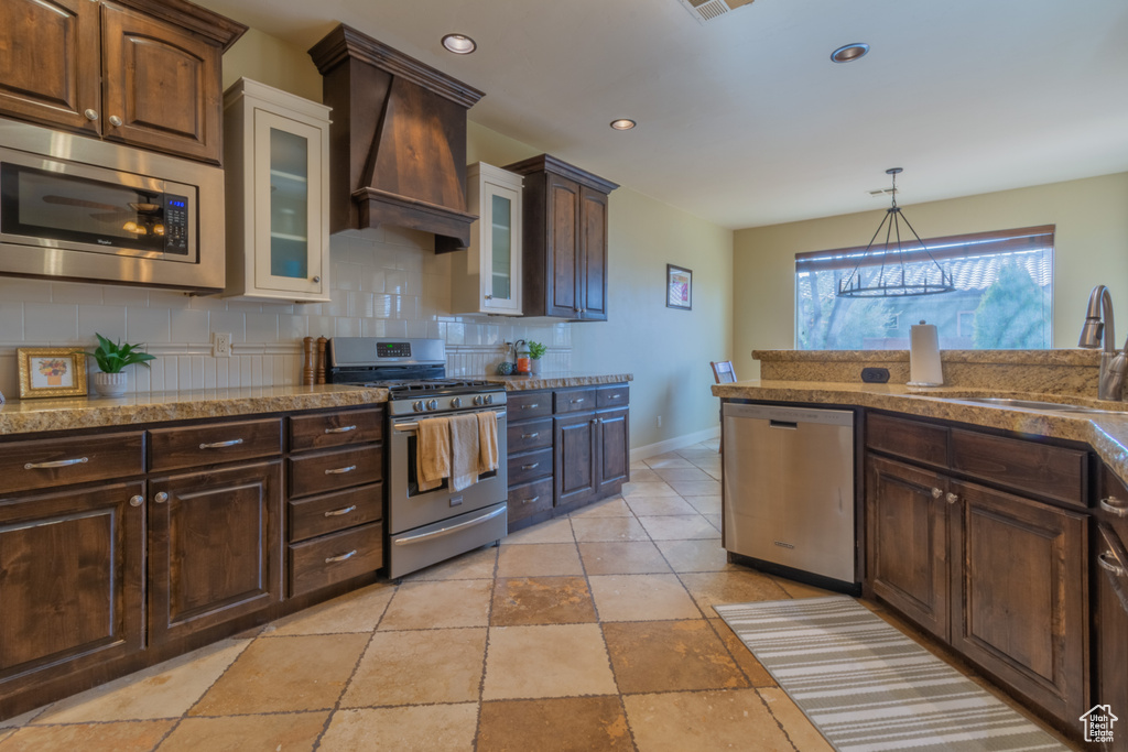 Kitchen with sink, hanging light fixtures, stainless steel appliances, premium range hood, and decorative backsplash