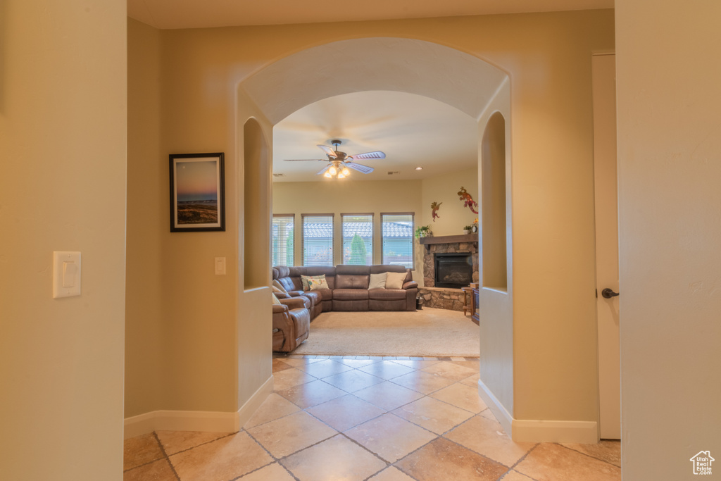 Tiled living room featuring a stone fireplace and ceiling fan