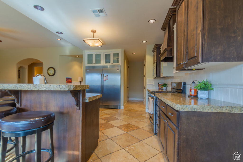 Kitchen featuring a breakfast bar, appliances with stainless steel finishes, decorative backsplash, and custom exhaust hood
