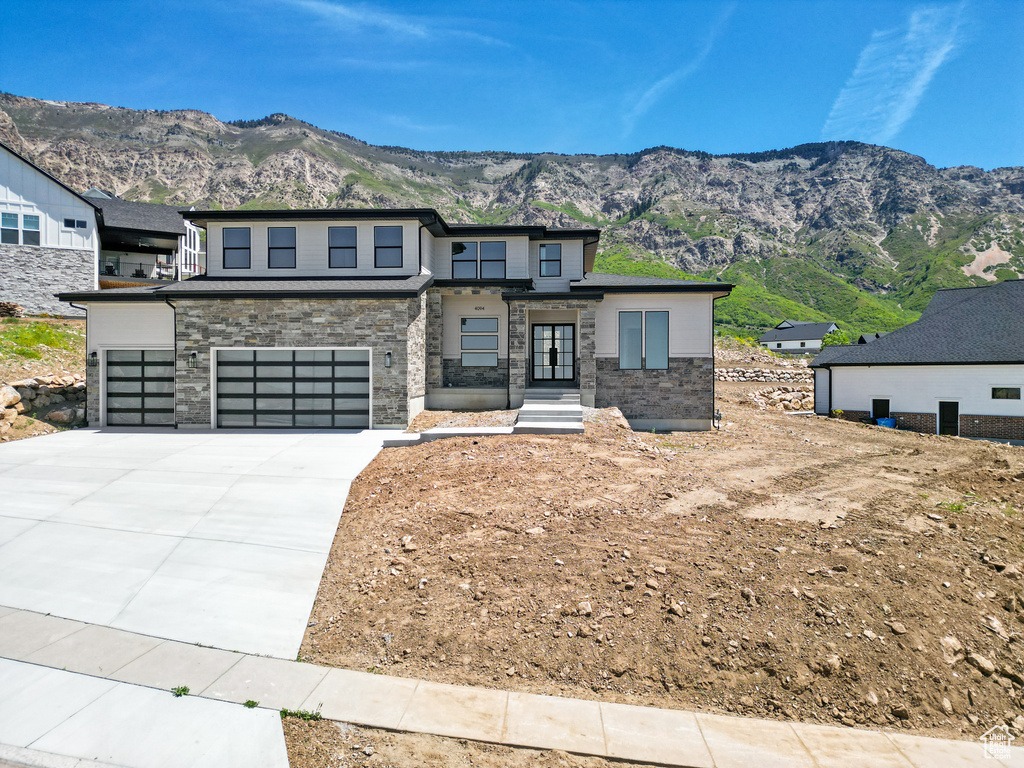 Modern home with a garage, a mountain view, concrete driveway, and stone siding