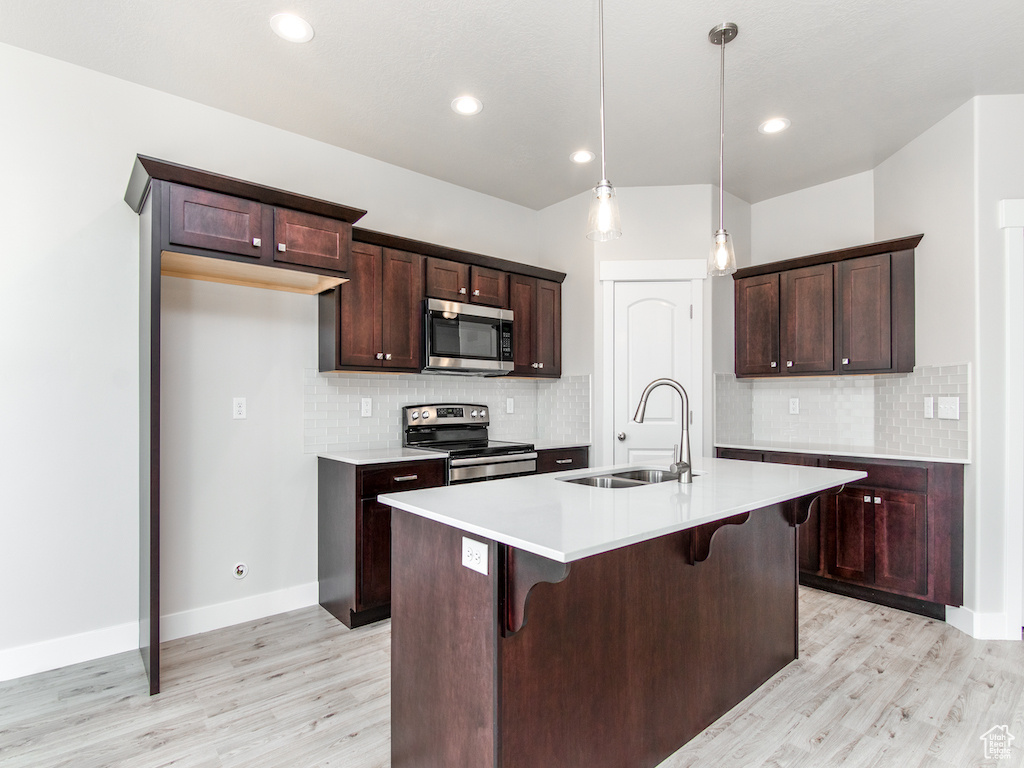 Kitchen with stainless steel appliances, sink, hanging light fixtures, a kitchen island with sink, and light hardwood / wood-style flooring