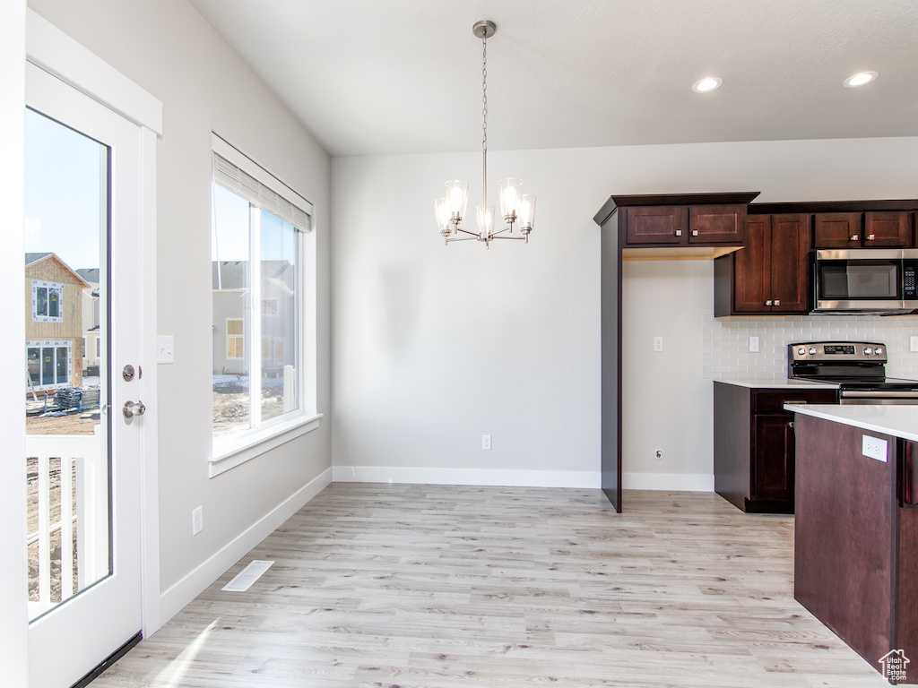 Kitchen with stainless steel appliances, a notable chandelier, pendant lighting, decorative backsplash, and light hardwood / wood-style flooring