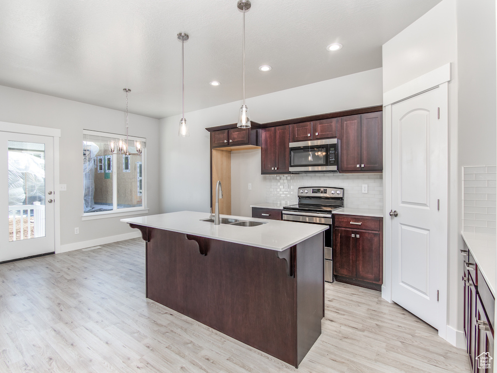 Kitchen with stainless steel appliances, hanging light fixtures, sink, and light hardwood / wood-style flooring