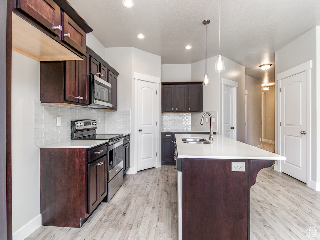 Kitchen featuring dark brown cabinetry, hanging light fixtures, sink, light hardwood / wood-style flooring, and appliances with stainless steel finishes