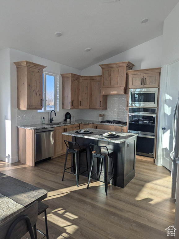 Kitchen featuring a kitchen bar, appliances with stainless steel finishes, dark hardwood / wood-style floors, a kitchen island, and lofted ceiling