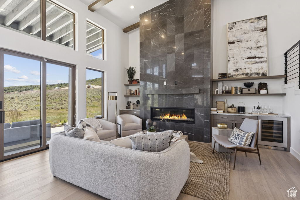 Living area featuring a towering ceiling, wine cooler, a high end fireplace, light wood-type flooring, and bar area