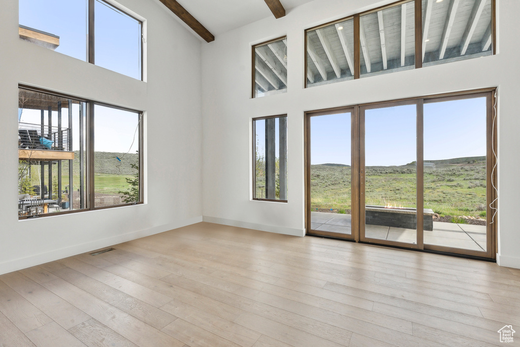 Empty room featuring beam ceiling, a high ceiling, wood finished floors, baseboards, and a mountain view