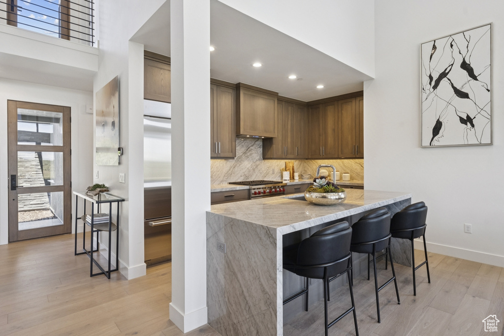 Kitchen featuring light stone countertops, light wood finished floors, tasteful backsplash, plenty of natural light, and a towering ceiling