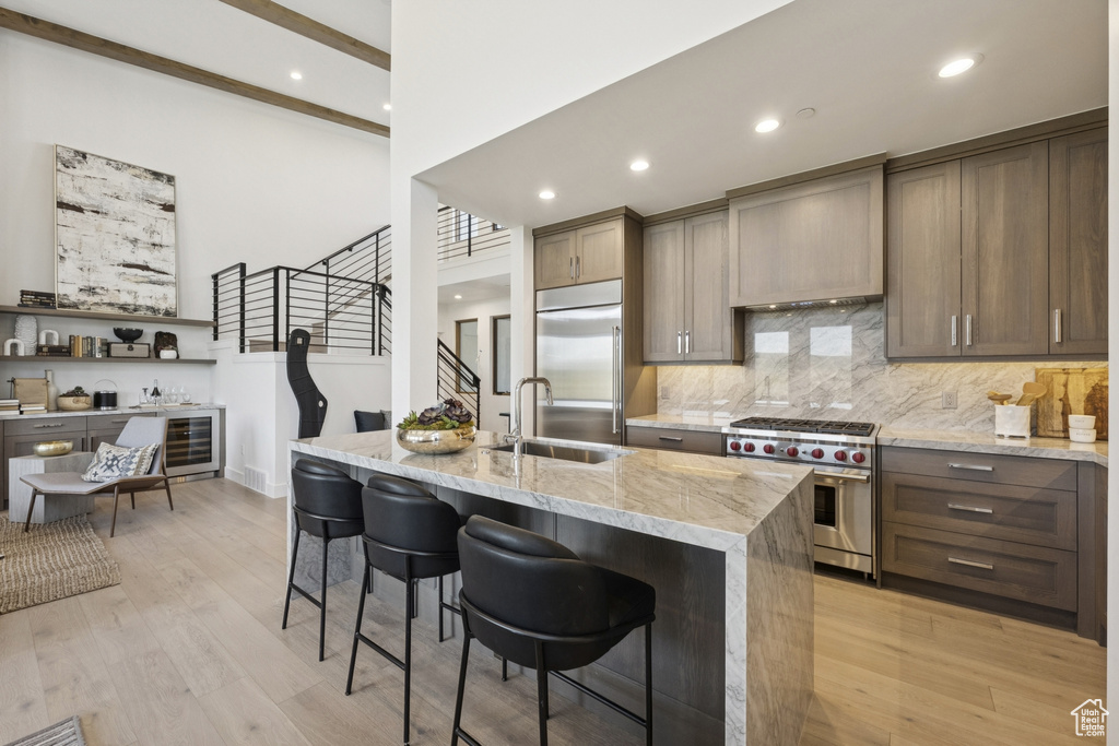 Kitchen featuring high quality appliances, light stone counters, tasteful backsplash, a breakfast bar, and light wood-style flooring