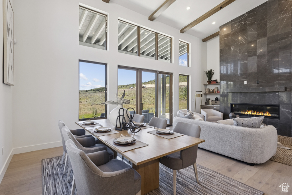 Dining area with beam ceiling, a high ceiling, wood finished floors, a tile fireplace, and recessed lighting