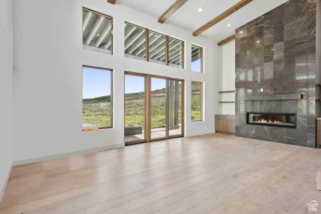 Unfurnished living room featuring beamed ceiling, a fireplace, a towering ceiling, wood finished floors, and baseboards