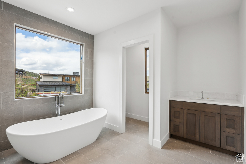 Bathroom featuring healthy amount of natural light, a soaking tub, baseboards, vanity, and tile walls