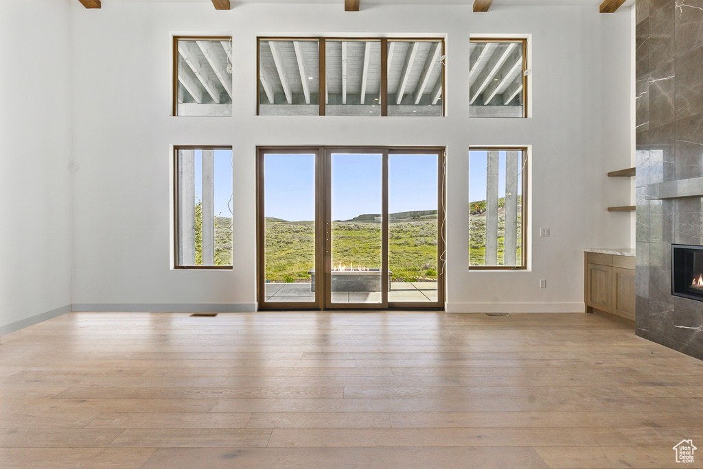 Unfurnished living room with a high ceiling, healthy amount of natural light, a fireplace, wood-type flooring, and beamed ceiling