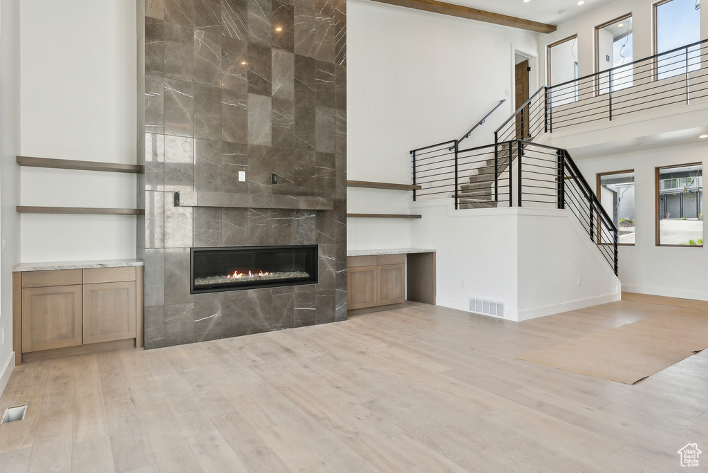 Unfurnished living room featuring a fireplace, stairway, light wood-style flooring, a towering ceiling, and baseboards