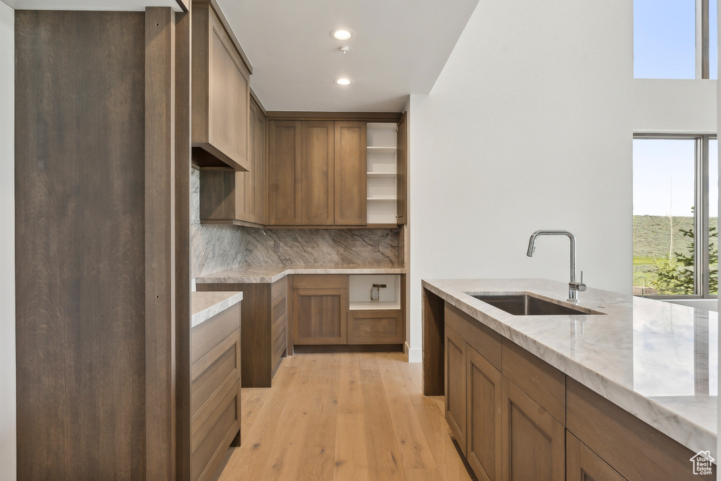 Kitchen with a sink, open shelves, backsplash, light wood-style flooring, and light stone countertops