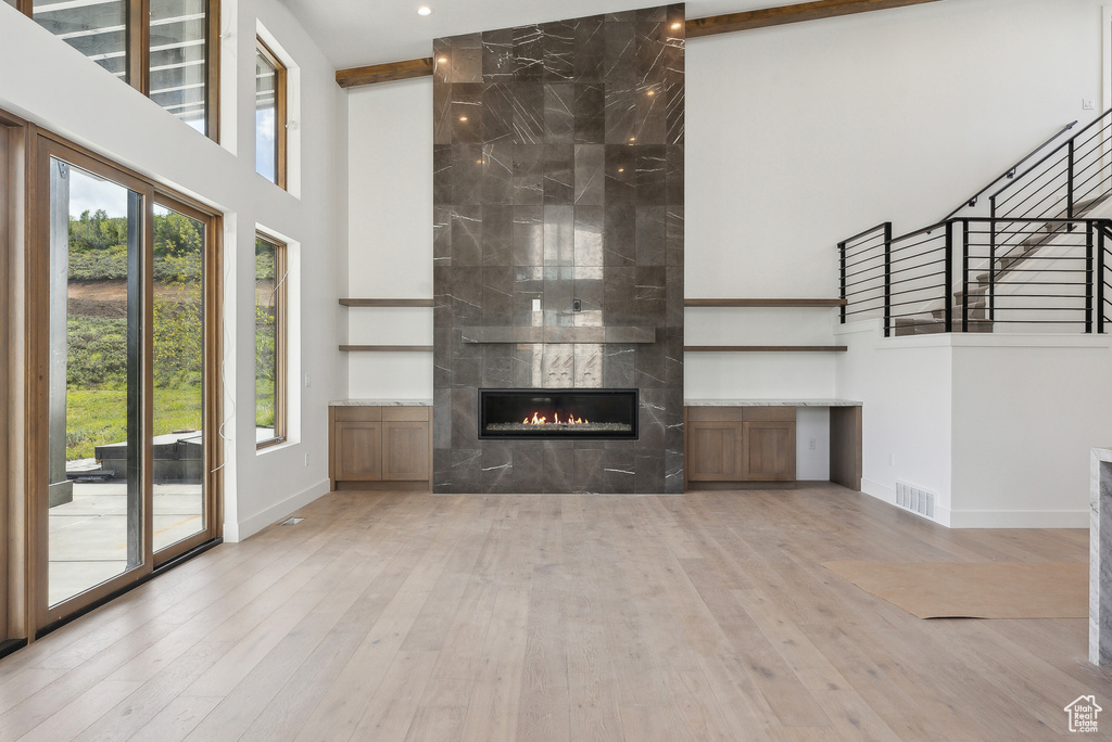 Unfurnished living room featuring a towering ceiling, baseboards, hardwood / wood-style flooring, a tiled fireplace, and stairs