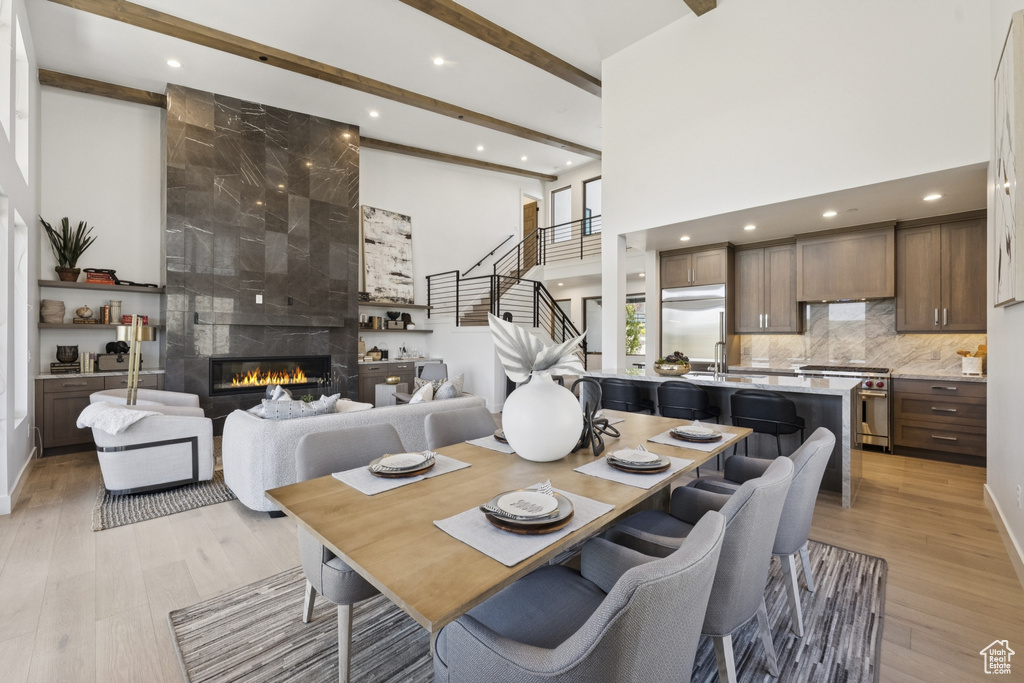 Dining room with recessed lighting, beam ceiling, light wood-style flooring, a towering ceiling, and a fireplace