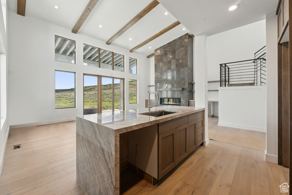 Kitchen with a sink, a kitchen island with sink, a large fireplace, open floor plan, and light stone countertops