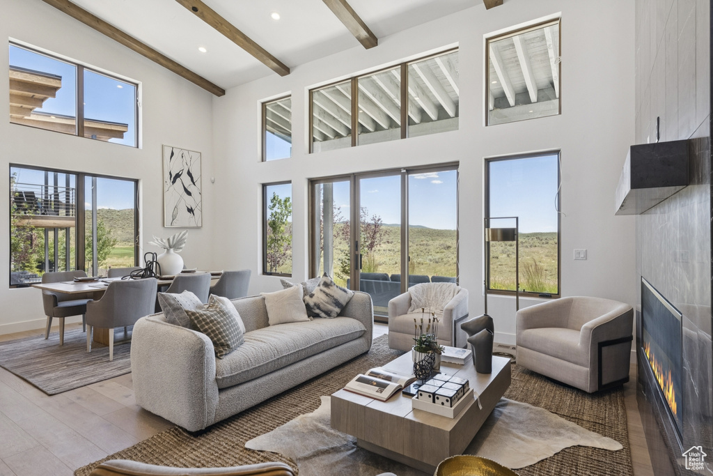 Living room with healthy amount of natural light, wood finished floors, beamed ceiling, a towering ceiling, and a large fireplace