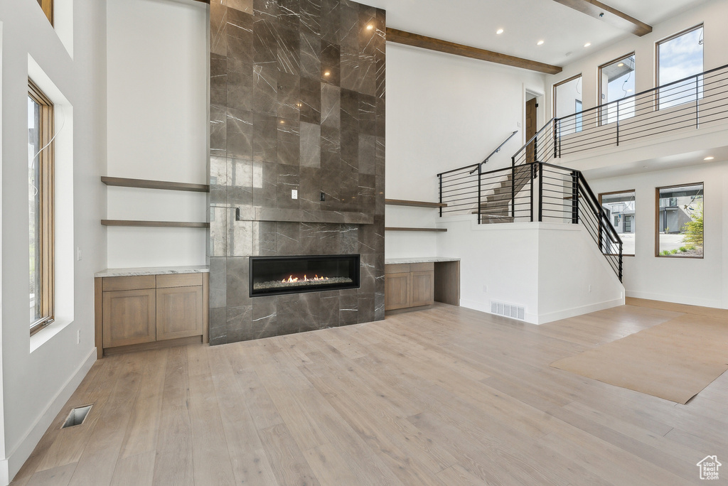 Unfurnished living room featuring wood finished floors, a tiled fireplace, a high ceiling, healthy amount of natural light, and stairs
