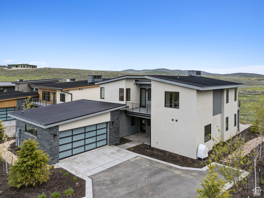 Modern home featuring stone siding, a balcony, stucco siding, driveway, and a mountain view