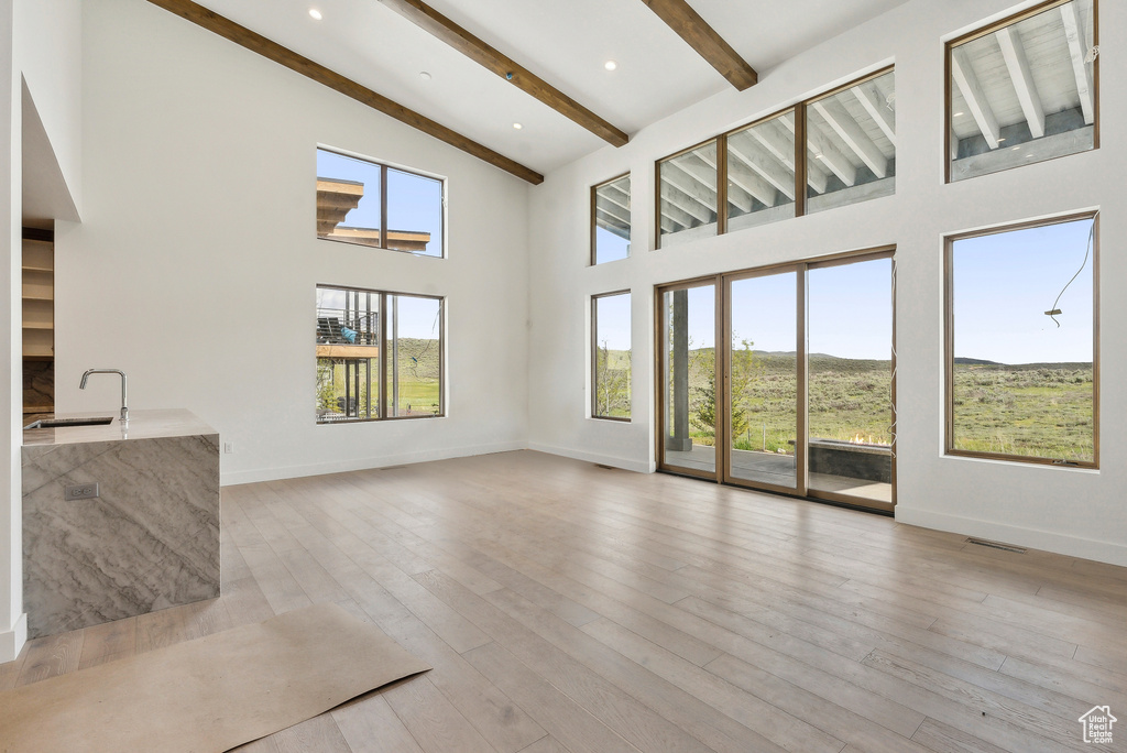 Unfurnished living room featuring beam ceiling, baseboards, a high ceiling, a sink, and light wood finished floors