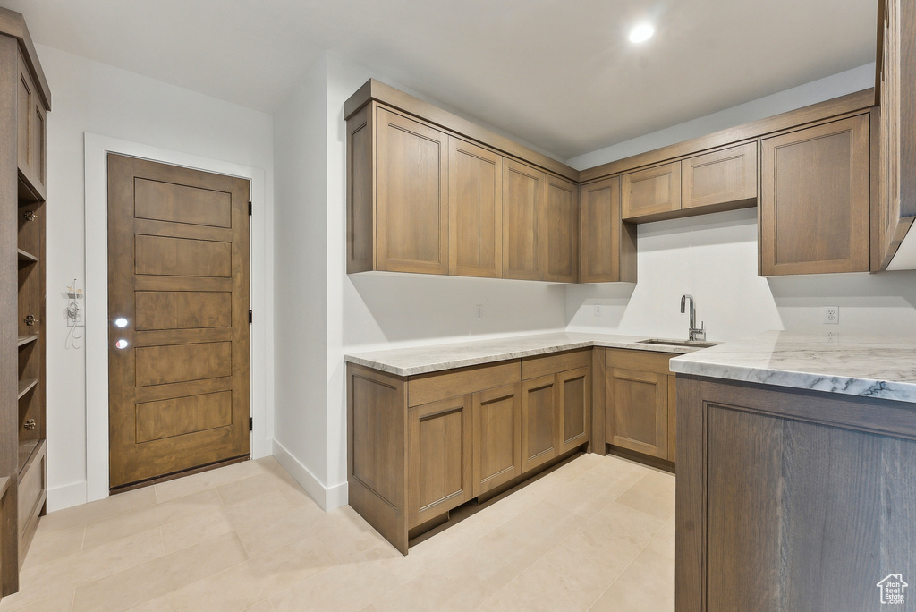 Kitchen with light stone counters, a sink, baseboards, brown cabinetry, and light tile patterned floors