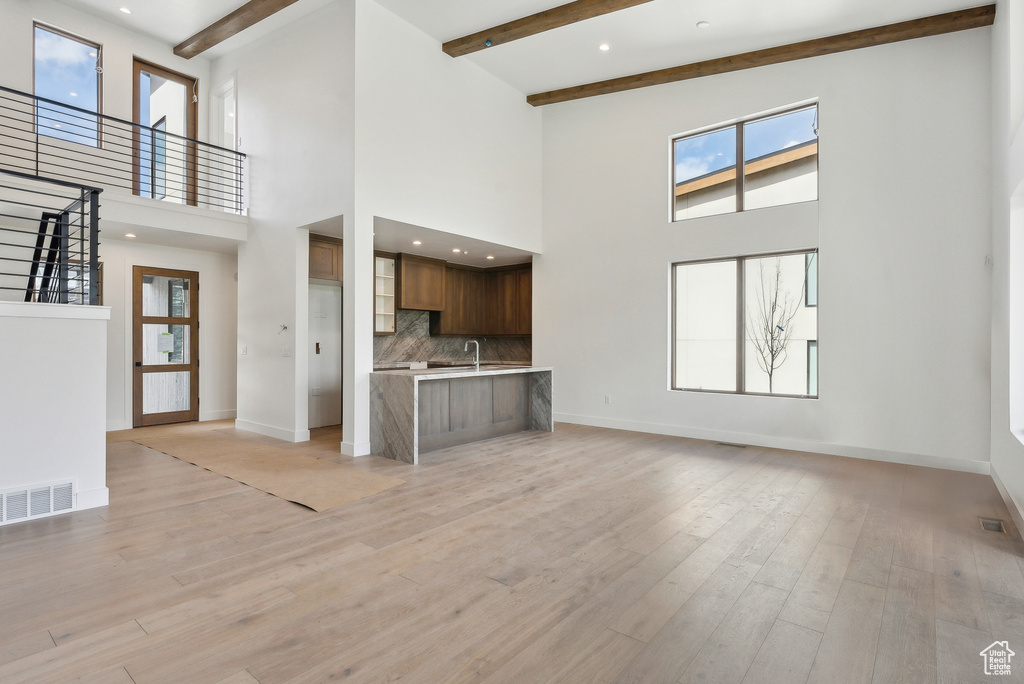 Unfurnished living room with plenty of natural light, baseboards, a high ceiling, beamed ceiling, and a sink